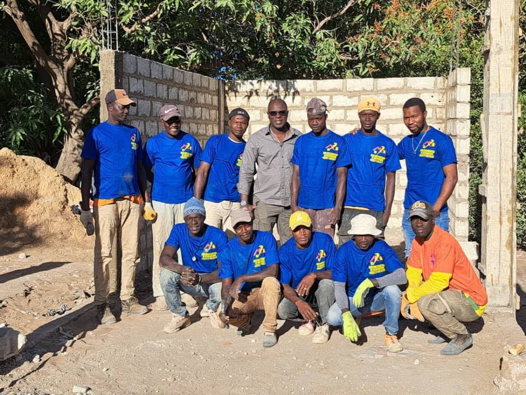 L'équipe CMR en tee-shirts bleus à l'effigie de l'entreprise, devant un mur en parpaings en cours de construction